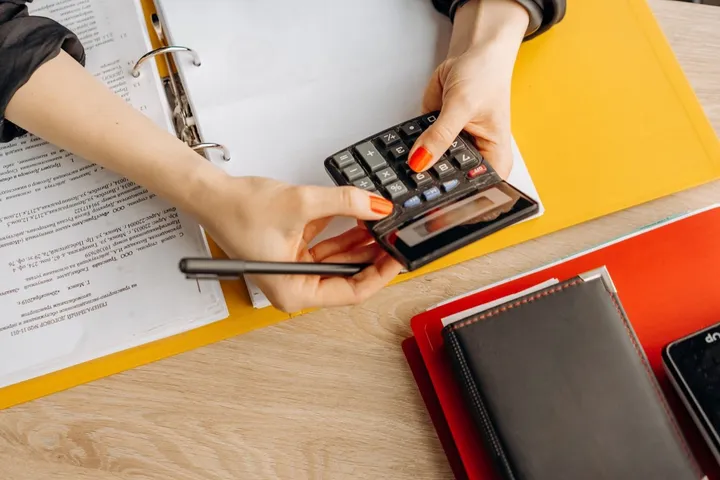 Mãos fazendo contas numa calculadora ao lado de pastas de documentos abertas
