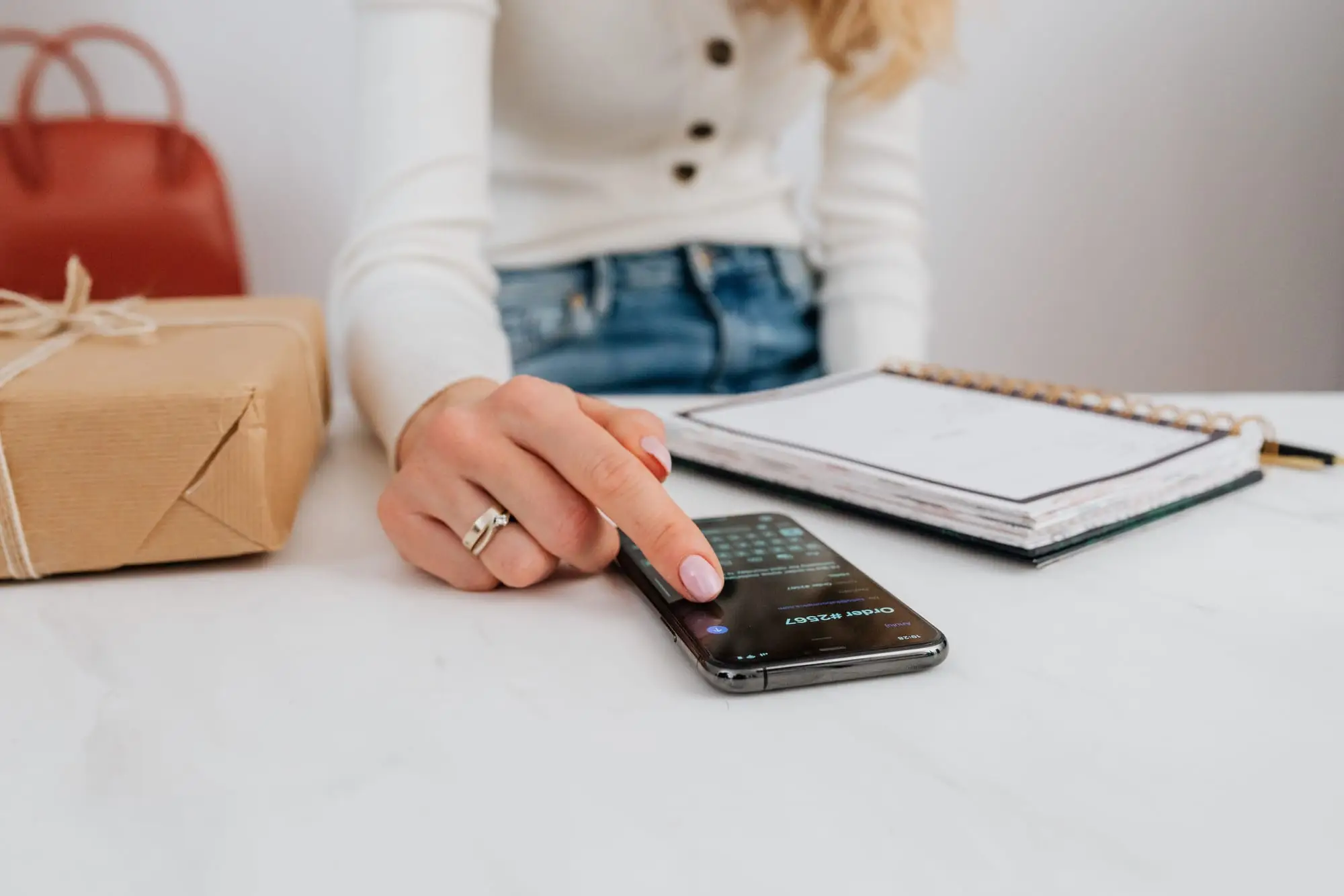 Mão tocando a tela de um celular sobre a mesa, ao lado de uma agenda aberta