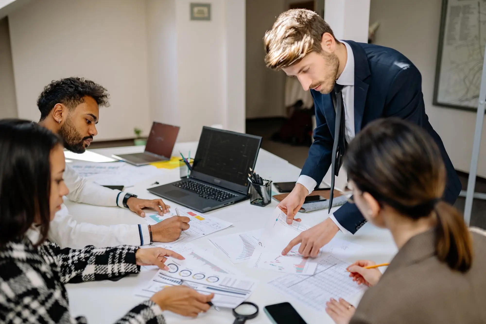 Quatro pessoas em volta de uma mesa com notebooks e relatórios, numa conversa de trabalho
