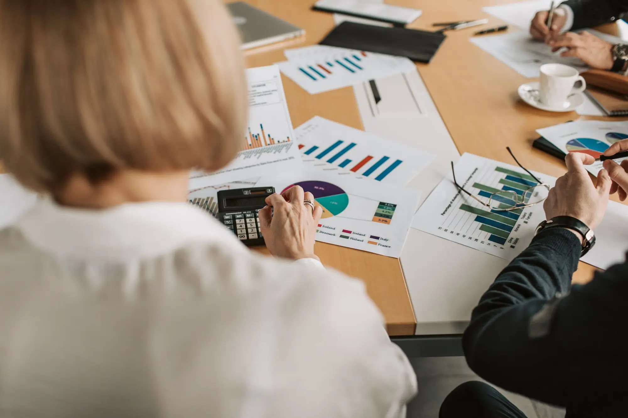 Mesa de reunião com gráficos impressos e calculadora, com duas pessoas revisando os números